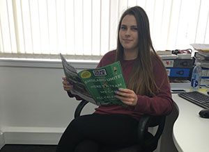 Big Issue Foundation volunteer Nina sitting at desk and holding Big Issue magazine